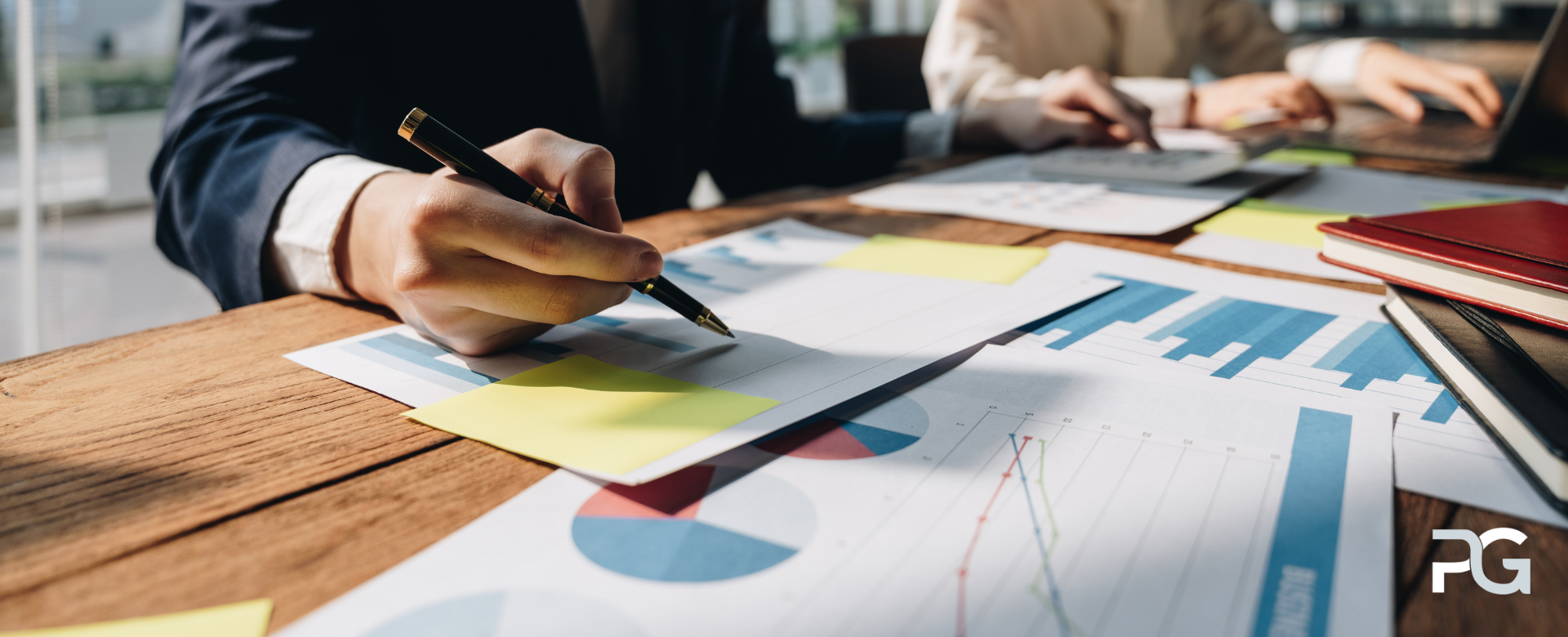 Professional reviewing charts and financial reports at a meeting table, writing notes on documents with graphs, data visuals, and sticky notes.