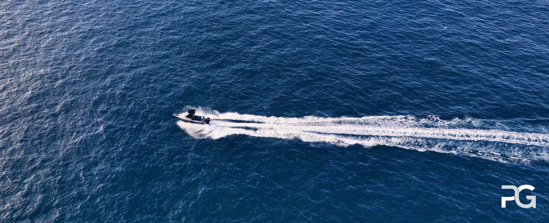 Alt text (100 characters): Speedboat cutting across deep blue water, leaving white wakes behind in an aerial ocean view.